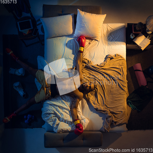 Image of Top view of young professional boxer, fighter sleeping at his bedroom in sportwear with gloves