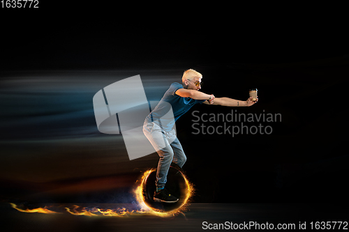 Image of Fast delivery service - deliveryman on unicycle driving with order in fire on dark background