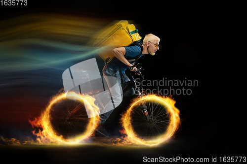 Image of Fast delivery service - deliveryman on bicycle driving with order in fire on dark background