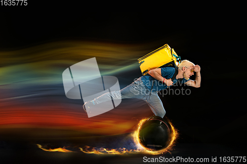 Image of Fast delivery service - deliveryman on unicycle driving with order in fire on dark background