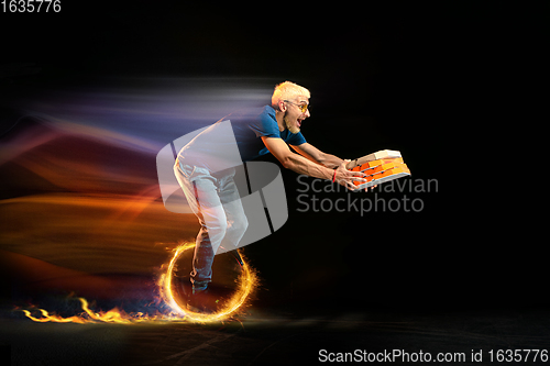 Image of Fast delivery service - deliveryman on unicycle driving with order in fire on dark background