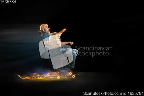 Image of Fast delivery service - deliveryman on chair driving with order in fire on dark background