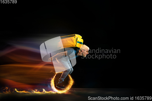 Image of Fast delivery service - deliveryman on unicycle driving with order in fire on dark background