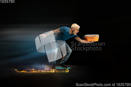Image of Fast delivery service - deliveryman on unicycle driving with order in fire on dark background