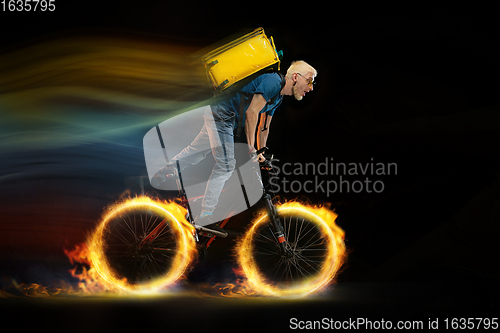 Image of Fast delivery service - deliveryman on bicycle driving with order in fire on dark background