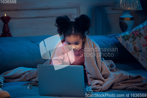 Image of Happy african-american little girl during video call with laptop and home devices, looks delighted and happy