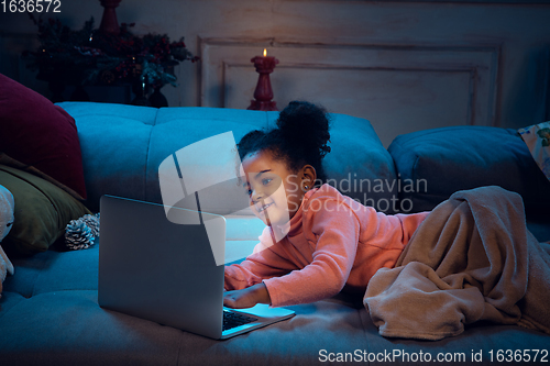 Image of Happy african-american little girl during video call with laptop and home devices, looks delighted and happy