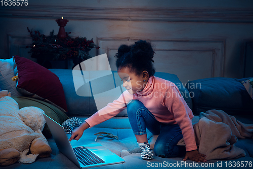 Image of Happy african-american little girl during video call with laptop and home devices, looks delighted and happy