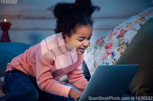 Image of Happy african-american little girl during video call with laptop and home devices, looks delighted and happy