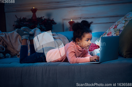 Image of Happy african-american little girl during video call with laptop and home devices, looks delighted and happy