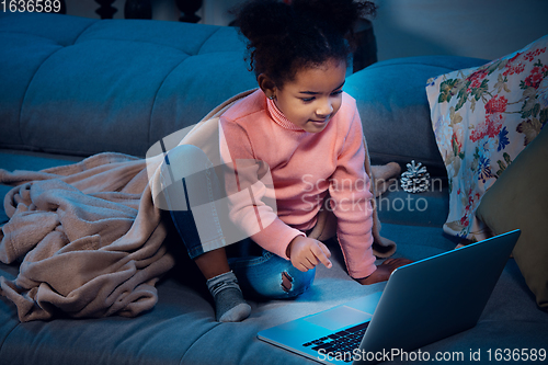 Image of Happy african-american little girl during video call with laptop and home devices, looks delighted and happy