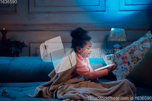 Image of Happy african-american little girl during video call with laptop and home devices, looks delighted and happy