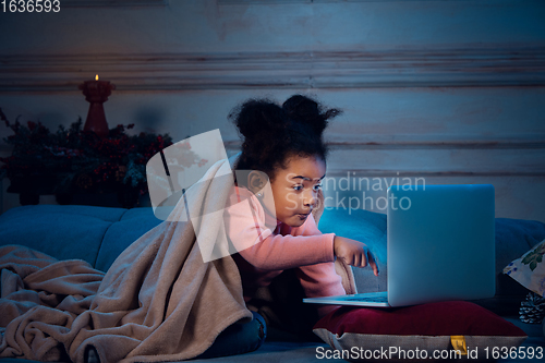 Image of Happy african-american little girl during video call with laptop and home devices, looks delighted and happy