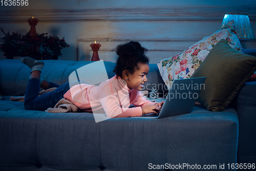 Image of Happy african-american little girl during video call with laptop and home devices, looks delighted and happy