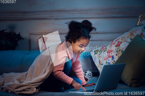 Image of Happy african-american little girl during video call with laptop and home devices, looks delighted and happy