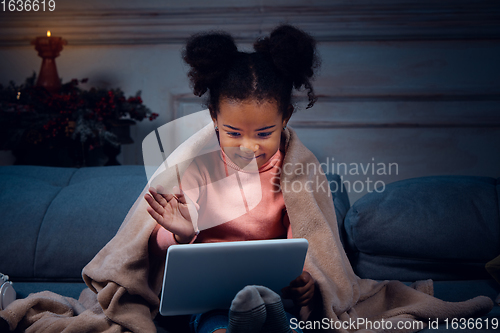 Image of Happy african-american little girl during video call with laptop and home devices, looks delighted and happy