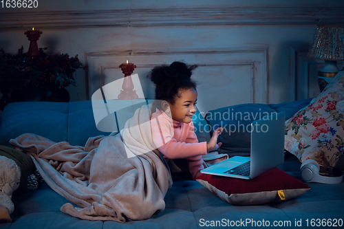 Image of Happy african-american little girl during video call with laptop and home devices, looks delighted and happy