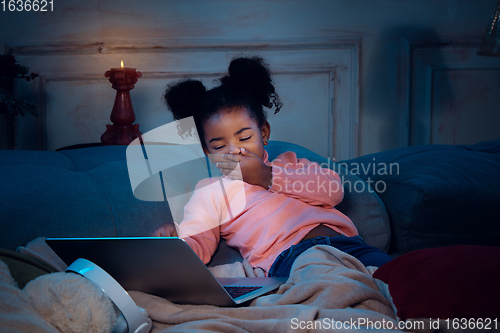 Image of Happy african-american little girl during video call with laptop and home devices, looks delighted and happy