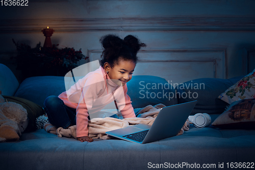 Image of Happy african-american little girl during video call with laptop and home devices, looks delighted and happy