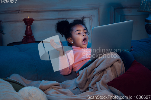 Image of Happy african-american little girl during video call with laptop and home devices, looks delighted and happy