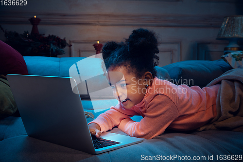 Image of Happy african-american little girl during video call with laptop and home devices, looks delighted and happy