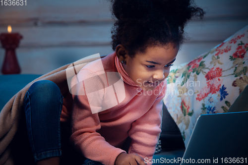 Image of Happy african-american little girl during video call with laptop and home devices, looks delighted and happy