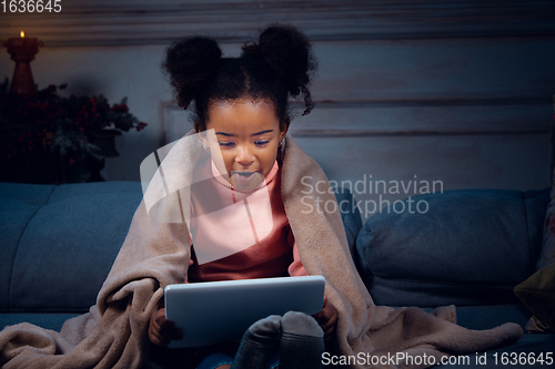 Image of Happy african-american little girl during video call with laptop and home devices, looks delighted and happy