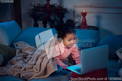 Image of Happy african-american little girl during video call with laptop and home devices, looks delighted and happy
