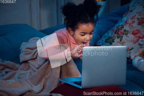 Image of Happy african-american little girl during video call with laptop and home devices, looks delighted and happy