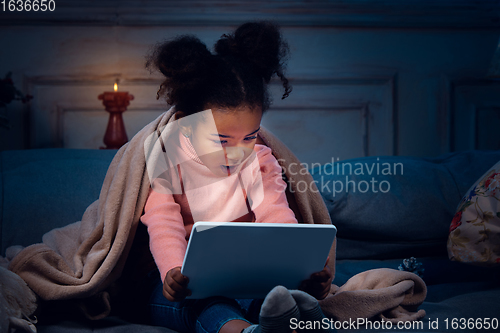 Image of Happy african-american little girl during video call with laptop and home devices, looks delighted and happy