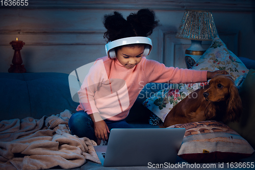 Image of Happy african-american little girl during video call with laptop and home devices, looks delighted and happy