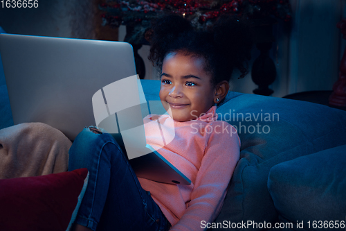 Image of Happy african-american little girl during video call with laptop and home devices, looks delighted and happy