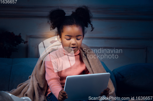 Image of Happy african-american little girl during video call with laptop and home devices, looks delighted and happy