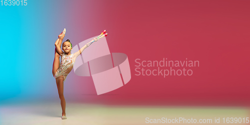 Image of Little caucasian girl, rhytmic gymnast training, performing isolated on gradient blue-red studio background in neon