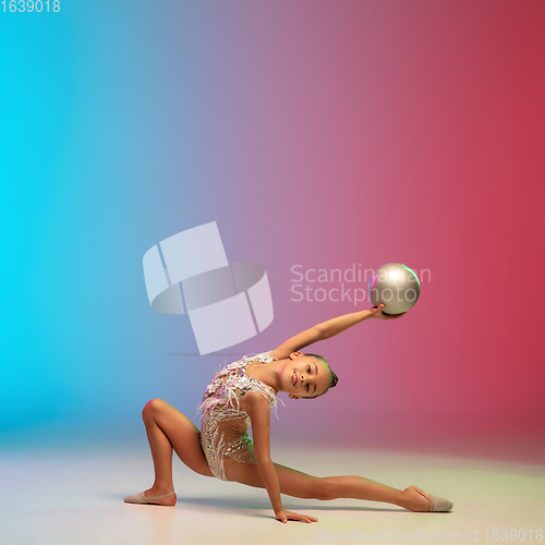 Image of Little caucasian girl, rhytmic gymnast training, performing isolated on gradient blue-red studio background in neon