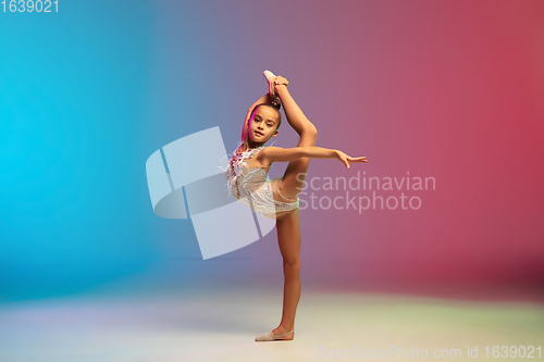 Image of Little caucasian girl, rhytmic gymnast training, performing isolated on gradient blue-red studio background in neon