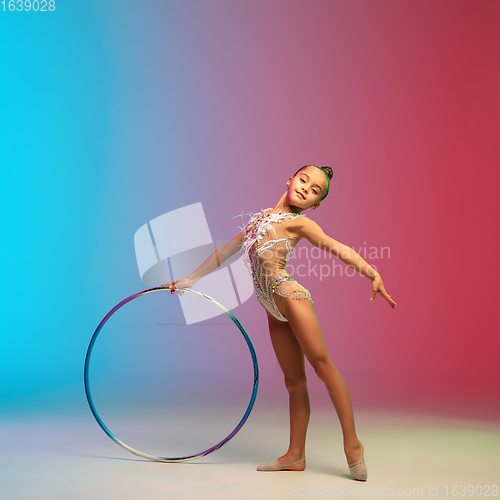 Image of Little caucasian girl, rhytmic gymnast training, performing isolated on gradient blue-red studio background in neon