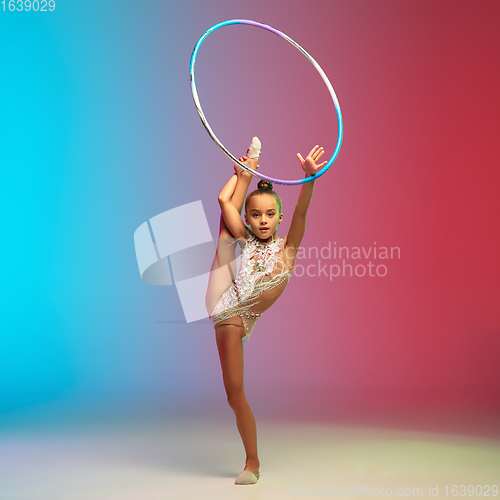 Image of Little caucasian girl, rhytmic gymnast training, performing isolated on gradient blue-red studio background in neon