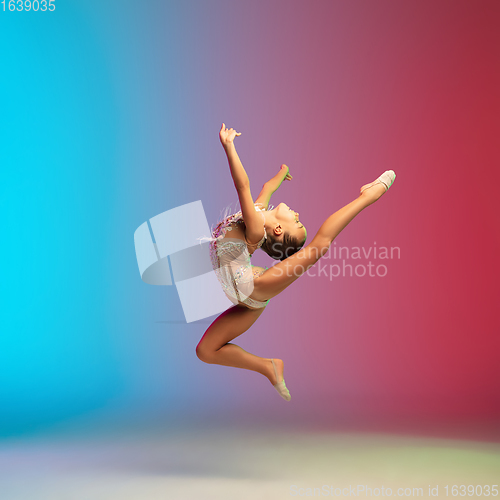 Image of Little caucasian girl, rhytmic gymnast training, performing isolated on gradient blue-red studio background in neon