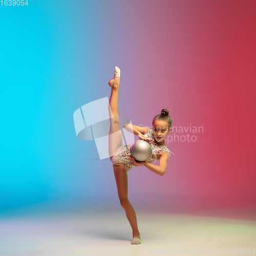 Image of Little caucasian girl, rhytmic gymnast training, performing isolated on gradient blue-red studio background in neon