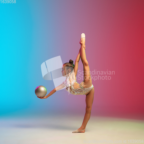 Image of Little caucasian girl, rhytmic gymnast training, performing isolated on gradient blue-red studio background in neon