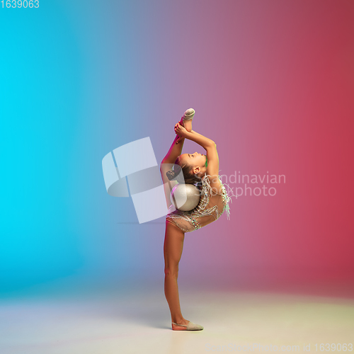 Image of Little caucasian girl, rhytmic gymnast training, performing isolated on gradient blue-red studio background in neon