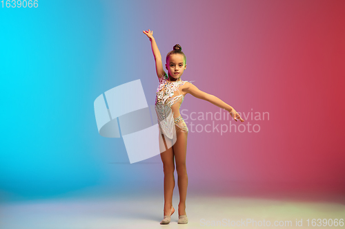 Image of Little caucasian girl, rhytmic gymnast training, performing isolated on gradient blue-red studio background in neon