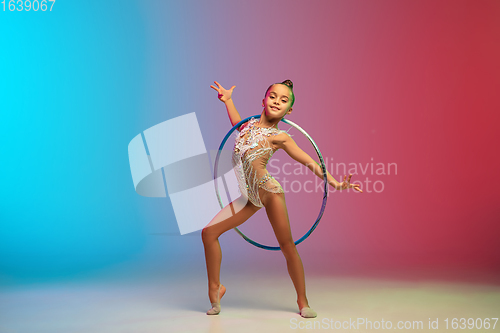 Image of Little caucasian girl, rhytmic gymnast training, performing isolated on gradient blue-red studio background in neon