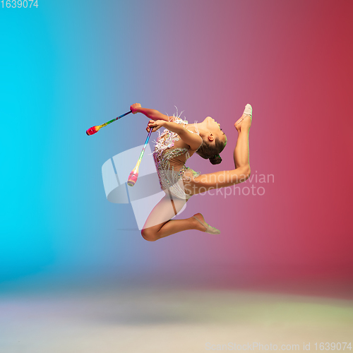 Image of Little caucasian girl, rhytmic gymnast training, performing isolated on gradient blue-red studio background in neon