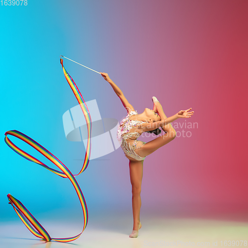 Image of Little caucasian girl, rhytmic gymnast training, performing isolated on gradient blue-red studio background in neon