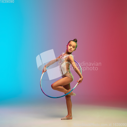 Image of Little caucasian girl, rhytmic gymnast training, performing isolated on gradient blue-red studio background in neon