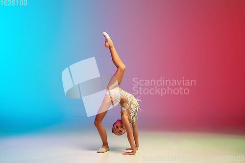 Image of Little caucasian girl, rhytmic gymnast training, performing isolated on gradient blue-red studio background in neon