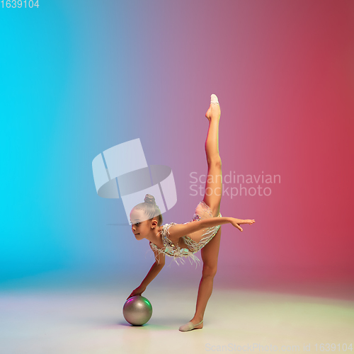 Image of Little caucasian girl, rhytmic gymnast training, performing isolated on gradient blue-red studio background in neon