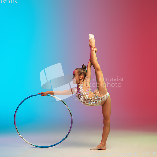 Image of Little caucasian girl, rhytmic gymnast training, performing isolated on gradient blue-red studio background in neon